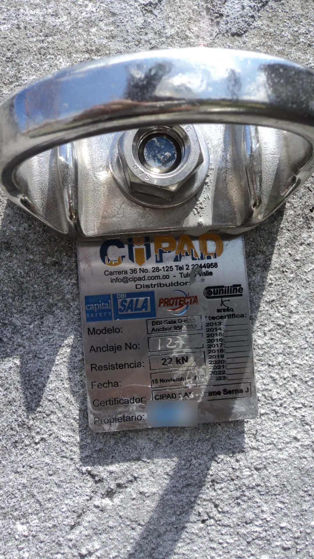 Placa de identificación de un punto de anclaje estructural con número, resistencia de 22 kN, fecha de certificación y retícula de recertificación anual