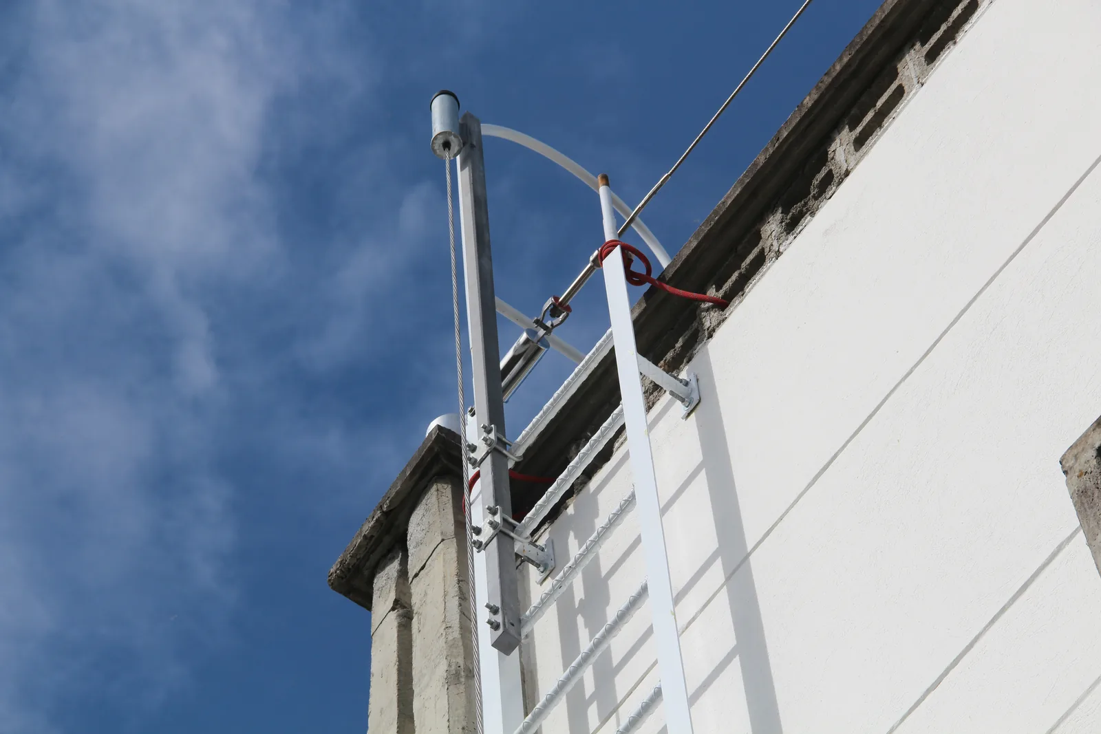 Extremo superior de una línea de vida vertical anclada a estructura, con tensor y cable de acero contra el cielo